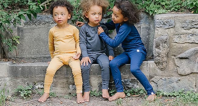 Three kids wearing Woolino Merino Wool Thermal Tops & Leggings in Honey, Charcoal, and Deep Blue.